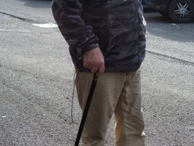 Macro 'nun yaşlı, tanınmayan bir adamın, sokakta yürüme bastonunun ahşap sapını tutarken çekilmiş fotoğrafı.