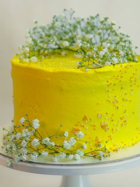 Beyaz arka planda yabani beyaz çiçekli sarı kutlama pastası.