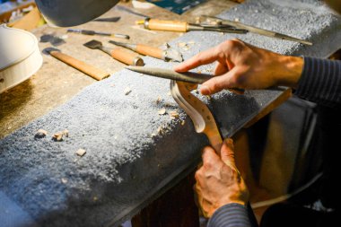 Luthier kemancı keman tomarı üzerinde çalışıyor, dikkatle kafa kazıyor ve şekillendiriyor.