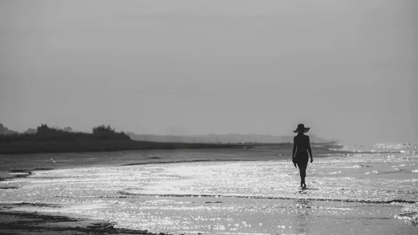 若い女性は砂浜でファッショナブルな服にポーズをとっています 背景に美しい海の風景 ブルネットモデル 背の高い 日焼けとスリム 白黒写真 — ストック写真