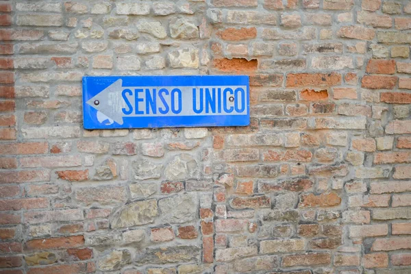 蓝色的单向意大利交通路标越过一堵古老的砖墙感情用事的文字 图库照片