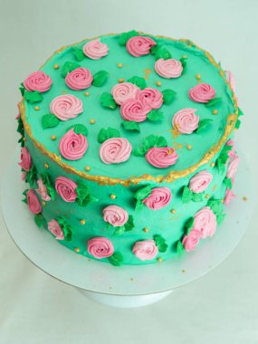 Stüdyoda izole edilmiş şekildeki süslemeleri süsleyen şeker hamuru gülleri ve incilerle kaplı yeşil kremalı pasta.