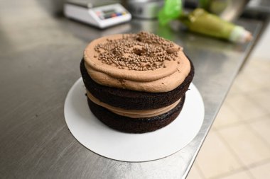 Profesyonel bir aşçının mutfağında katmanlı koyu çikolatalı pasta ve krema hazırlığı.