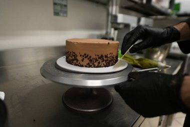 Pasta şefi kremayı yumuşatıyor. Donmuş katmanlı, çikolatalı pasta. Profesyonel mutfağın yüksek çözünürlükte resmi.