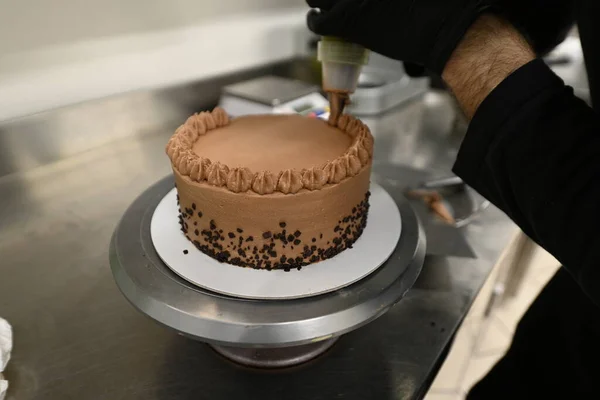 pastry chef using piping bag filled with butter cream to decorate a brown dark chocolate frosted layered creamy cup cake