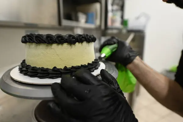 pastry chef using piping bag filled with butter cream to decorate a frosted layered creamy cup cake