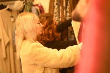 Sarışın genç kadın ve kızıl saçlı en iyi arkadaş moda mağazasında kışın indirimli kıyafet seçiyorlar.