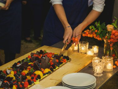 Ahşap bir masa taze pişmiş kısa hamurlu pastayla sunulur. Renkli ve taze meyvelerle kaplı büyük bir pasta. Meyve, kivi ve şeftali gibi..