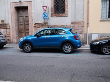 Cremona, İtalya - 27 Mayıs 2024 Fiat 500 x 4x4 canlı mavi araba büyüleyici italyan caddesinde park halinde paralı bir arsaya park edildi. Fiat mimarinin arka planına karşı çıkıyor.