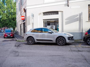 Cremona, İtalya - 27 Mayıs 2024 Porsche Macan mat gri SUV, İtalya 'da dar bir caddede park halinde, kentsel alanlarda araba kullanmanın ve park yeri bulmanın zorluklarını vurguluyor.