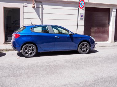Cremona, İtalya - 27 Mayıs 2024 Blue alfa romeo giulietta İtalya 'da dar bir sokağa park edilmiş, güneş ışığıyla yıkanmış. İtalya 'da tipik bir sokak sahnesi gösteriliyor. Park levhası yok ve garaj kapısı var.