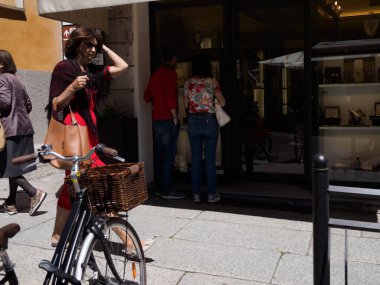 Cremona, İtalya - 27 Mayıs 2024 Turistler İtalya 'da bir şehir caddesinde yürürken, bir mağazanın penceresine bakmak için durdular. Bir kadın bisikleti sepetle itiyor.