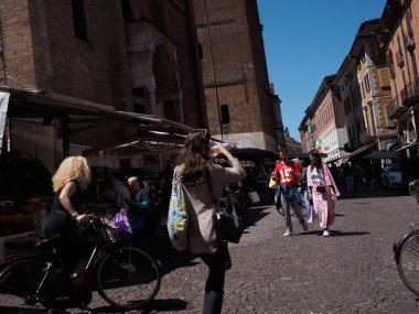 Cremona, İtalya - 27 Mayıs 2024 Turistler ve yerliler güneşli bir günün tadını çıkarıyorlar, İtalya 'da bir pazarda dolaşıyorlar. Pazara bakan uzun bir tuğla kule var.
