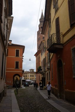 Cremona, İtalya - Haziran 2024 Ziyaretçiler ve sakinleri bulutlu bir günde hareketli binalar ve uzak bir kuleyle dolu tuhaf bir ara sokakta geziniyorlar