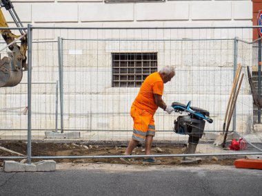 Cremona, İtalya - 10 Haziran 2024 İnşaat işçisi, inşaat alanında portakal rengi iş kıyafeti giyiyor.