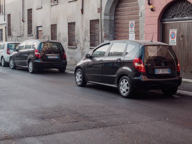 Cremona, İtalya - 10 Haziran 2024 İtalya 'da bir İtalyan köyünün antika bir sokağına park edilmiş iki parlak siyah araba, Avrupa' da şehir otoparkına örnek teşkil ediyor.