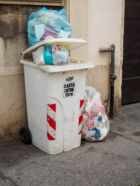 Cremona, İtalya - 10 Haziran 2024 Kentte kirli bir kaldırımda oturan çöp torbalarıyla dolu beyaz çöp kutusu