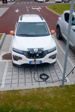 Cremona, İtalya - 15 Haziran 2024 Dacia White elektrikli otomobili şehir ortamında bir kamu şarj istasyonunda şarj oluyor.