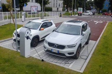 Cremona, İtalya - 15 Haziran 2024 Dacia ve Volvo Güneşli bir günde elektrik kablolarına bağlı iki elektrikli araç