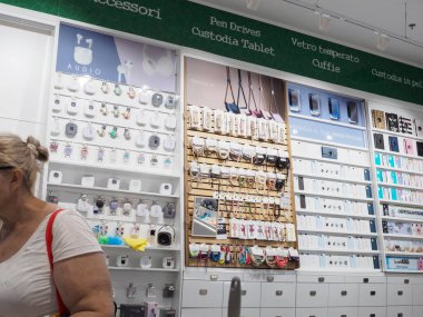 Cremona, İtalya 19 Temmuz 2024. Bir kadın bir elektronik mağazasından telefon aksesuarı alıyor ve farklı ürünlerden oluşan bir duvara bakıyor.