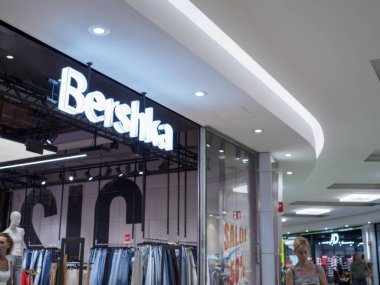 Cremona, Italy July 19th 2024 Customer walking in shopping mall passing by bershka clothing store with bright illuminated sign clipart