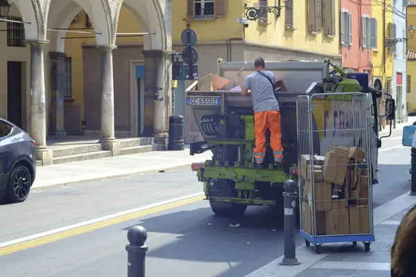 stock image Parma, Italy July 24th 2024 Garbage man working on a waste collection truck, throwing cardboard boxes into a container on a sunny day in an italian town