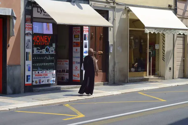 Stock image Parma, Italy July 24th 2024 A muslim woman is walking down a city sidewalk, passing by storefronts on a sunny summer day