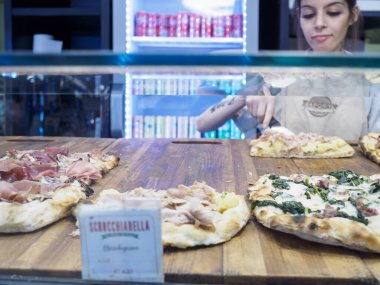 Cremona, İtalya 29 Temmuz 2024 Bir bayan tezgahtar pizza dilimleri hazırlıyor, onları cam ön vitrindeki vitrindeki tahta tahtalara yerleştiriyor.