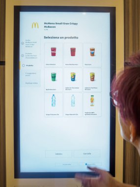Cremona, İtalya 29 Temmuz 2024 bir kadın fast food restoranında modern dijital servis panelini yemek siparişi vermek için kullanıyor.