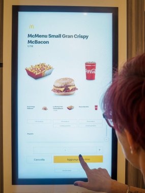 Cremona, İtalya 29 Temmuz 2024 bir kadın fast food restoranında yemek siparişi vermek için self servis terminalini kullanıyor.