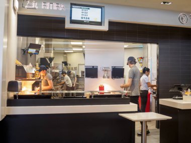 Cremona, İtalya 29 Temmuz 2024 Yoğun fast food işçileri aç müşteriler için alevler, dijital menüler ve hızlı servis yapan modern bir mutfakta yemek hazırlıyorlar.