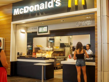 Cremona, İtalya. 29 Temmuz 2024. Meşgul bir McDonald 's tezgahında yemek sipariş eden bir kadın. Etrafı lezzetli yemeklerini bekleyen heyecanlı müşterilerle çevrili.