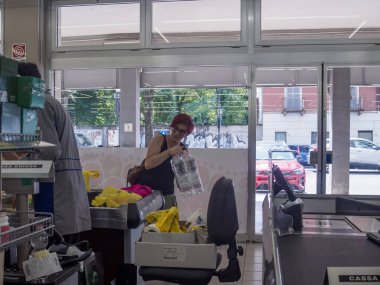 Cremona, İtalya 29 Temmuz 2024 Müşteri arka planda bir tezgahtar çalışırken bir marketin kasasındaki bir alışveriş çantasına şişe su koyuyor.