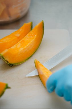 Bir şefin, taze kavunu kesme tahtasıyla parçalara ayırdığı bir sahne. Sulu portakal meyveleri lezzetli bir yaz yemeği için hazırlanıyor.