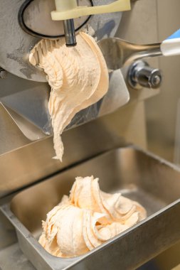 Makineden metal bir konteynıra yeni yapılmış dondurmanın yakın çekim görüntüsü. Dondurmanın kremalı dokusu ve kıvrımları görülebilir, pürüzsüz tutarlılığını sergiliyor..