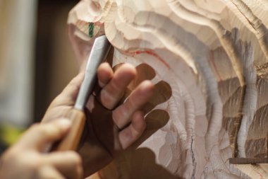 Esnaf keskiyle ahşap oyuyor, rahat bir atölyede karmaşık desenler ve dokular oluşturuyor. Ahşap heykel şekil alır, geleneksel ahşap işleme becerilerini sergiler.