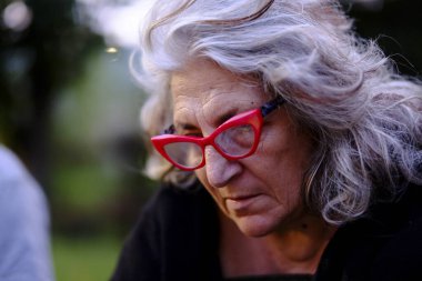 Gri saçlı ve kırmızı gözlüklü düşünceli son sınıf öğrencisi bir kadın yakın plan bir portrede zarafet ve bilgelik yayar.