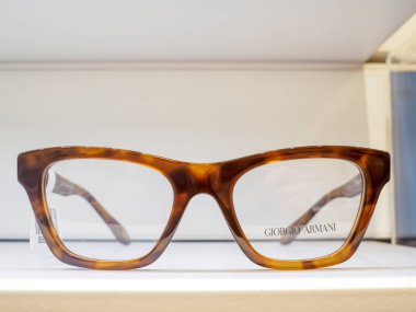 Kaplumbağa desenli bir çift Giorgio Armani gözlük beyaz bir yüzey üzerinde dinleniyor, muhtemelen bir gözlükçünün dükkanında bir vitrin rafı.