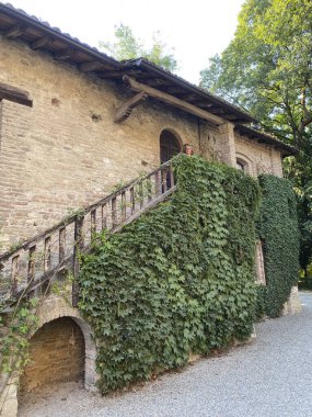 Grazzano VIsconti, İtalya 31 Ağustos 2023 Sarmaşık kaplı bir tuğla evin balkonunda duran bir kadın manzaranın tadını çıkarıyor.