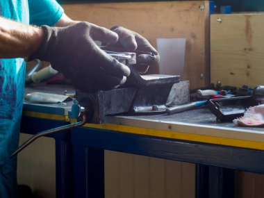 Koruyucu eldiven giyen tamirci araba parçalarını dikkatlice inceliyor. Tamir atölyesinde sağlam bir tezgah kullanıyor.