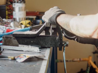 Eldiven giyen bisiklet tamircisi, tamirhanesinde bisiklet iskeleti üzerinde çalışırken bir metal parçasını tutmak için mengene kullanıyor.