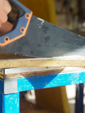 İnşaat işçisi ustalıkla ahşap tahtayı testereyle kesiyor, masadan düşen tahta tozu, el işçiliği ve marangozluk işçiliği sergiliyor.