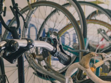 Bisiklet teçhizatıyla çevrili işlek bir tamirhanedeki klasik bisiklet gidonunun kapağı. Nostaljik atmosfer, kentsel çevre dostu ortamlarda bakım çalışmaları yakalıyor