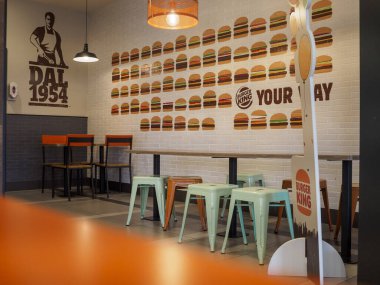 Cremona, İtalya 26 Eylül 2024 Turuncu ve yeşil metal sandalyeleri ve ahşap masaları olan modern bir fast food restoranının içi boş.