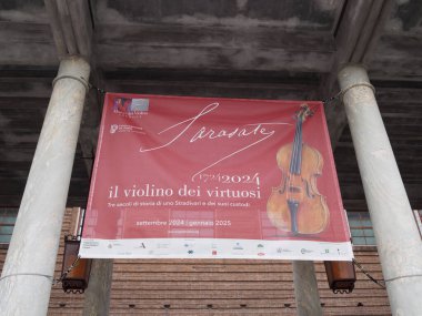 Cremona, Lombardy, İtalya 14 Ekim 2024 Kırmızı bayrak iki kolon arasında asılı bir stradivari keman sergisi, İtalyan kültür mirasını keman müzesinde tanıtmak