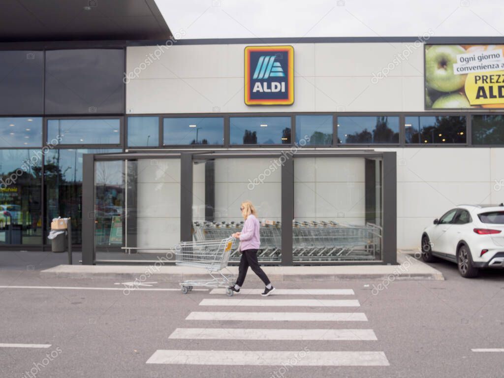 Cremona, Lombardy, Italy October 14th 2024 A woman is crossing the crosswalk pushing an empty shopping cart after shopping at the aldi supermarket