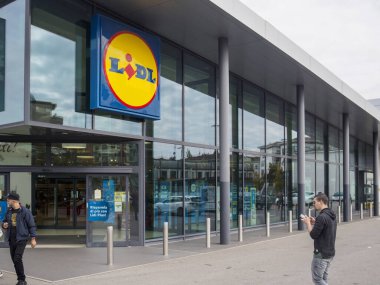 Cremona, Lombardy, İtalya 14 Ekim 2024 Müşteriler bulutlu bir günde kenti yansıtan büyük pencereli küçük bir süpermarketin girişinde yürüyorlar.