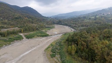 Lago di Mignano, Val Tolla, PC, İtalya - 12 Ekim 2024 Sonbaharda ağaçlar ve tepelerle çevrili bir vadiden geçen neredeyse kuru bir Arda nehir yatağının havadan görüntüsü. 