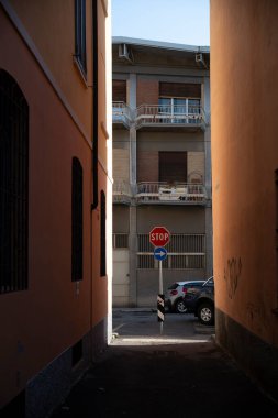 Cremona, Lombardy, İtalya 15 Ekim 2024 Güneşli bir günde arka planda arabaların park ettiği dar bir sokakta dur işareti var.