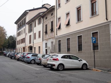 Cremona, Lombardy, İtalya. 15 Ekim 2024. Beyaz araba, apartman binaları ve park halindeki diğer arabaların bulunduğu bir park alanının yakınına park ediyor.